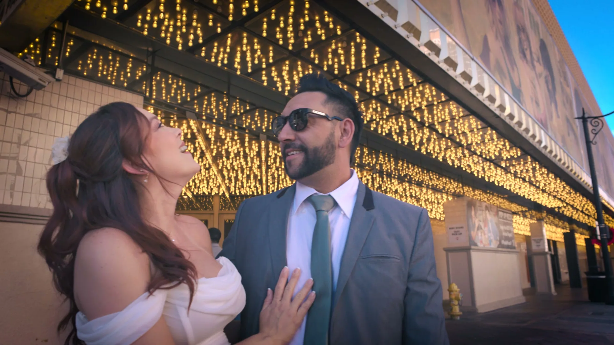 A couple laughing together beneath a canopy of gold lights